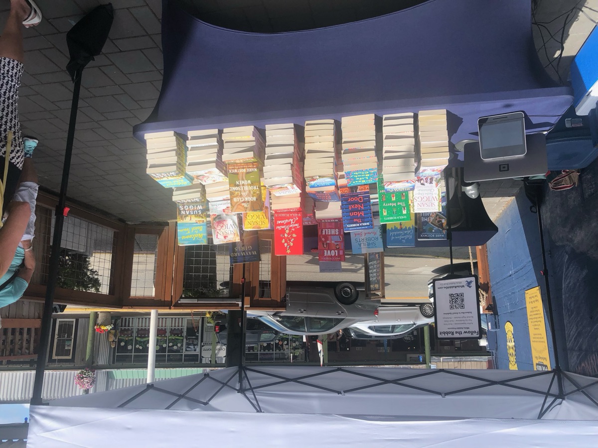 A table under a white canopy, stacked with paperback books in front of a street.