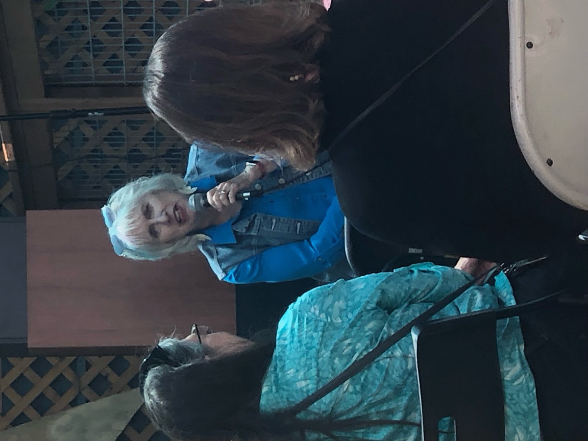 An author with white hair and a blue shirt speaking into a microphone.